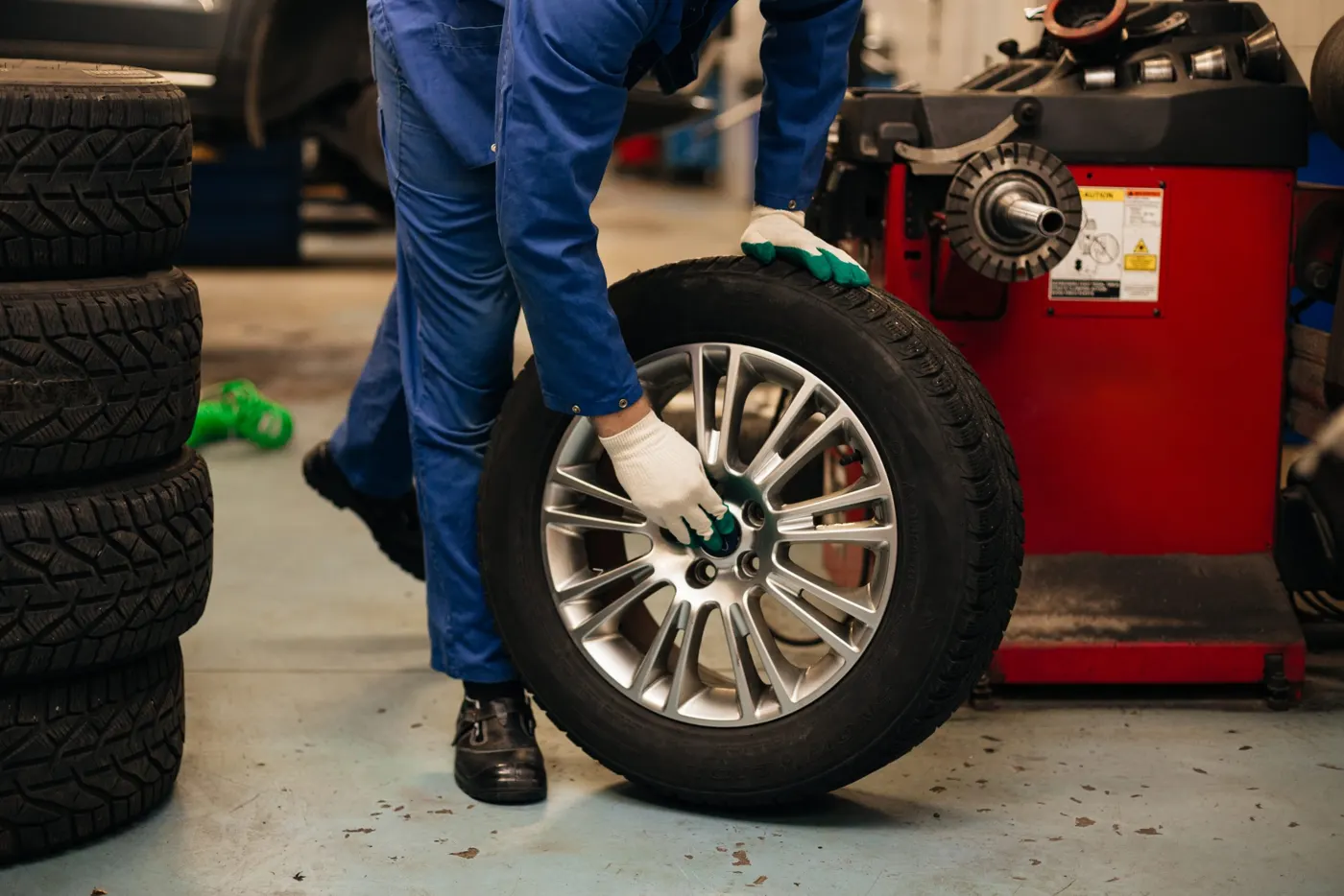 A technician holding a wheel in front of a wheel balancer in a tire bay (general scene)